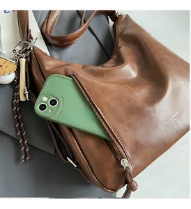 Detail of vintage brown leather tote showing a front zipper pocket with a smartphone
