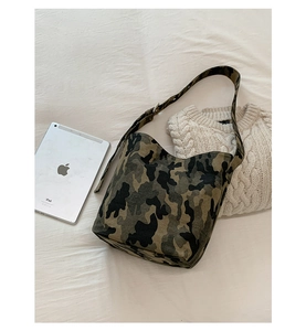 Close-up of military camouflage canvas tote bag with wide shoulder strap on beige fabric