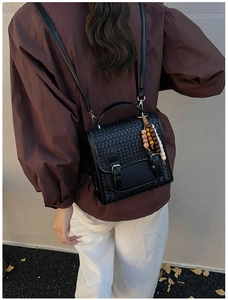 Detail of black woven leather backpack featuring flap closure and colorful beaded charm