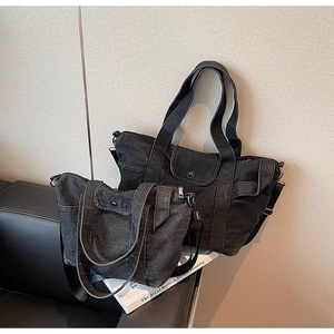 Detail of black denim tote bags in two sizes with white stitching on leather sofa