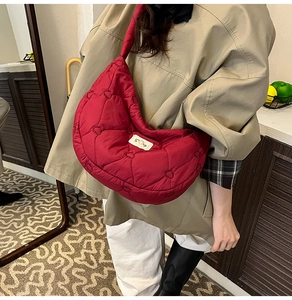 Detail of red heart-quilted puffer crescent bag with a minimalist brand label on surface
