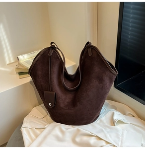 Detailed texture of dark brown suede tote bag with wavy opening on white linen cloth