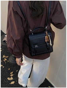 Detail of black woven PU leather backpack with bohemian bead charm on an autumn street