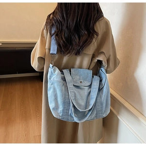 Detail of light blue denim tote bag featuring an adjustable strap and front pocket
