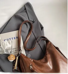 Detail of a brown faux leather hobo tote with a unique baseball glove charm and side zipper