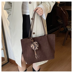 Detail of dark brown suede tote bag featuring a leopard print plush charm and tassel