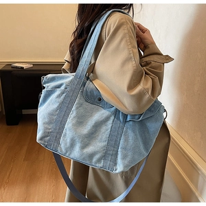 Detail of light blue denim tote bag showing wide handles and adjustable crossbody strap