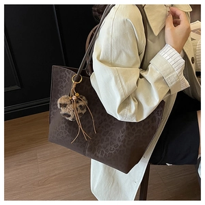 Detail view of large leopard print tote bag with a heart-shaped plush pendant and tassels