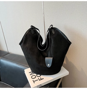Detail of black suede bucket bag with leather trim on white book and leather sofa