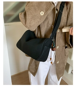 Detail der schwarzen Wildleder-Zylindertasche mit einem grünen Pflanzenanhänger-Accessoire