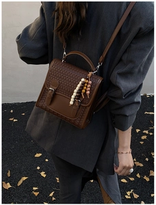 Close-up of brown woven leather crossbody bag with beaded tassel and flap closure