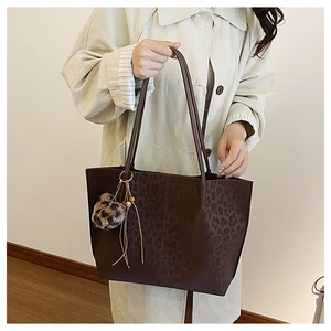 Detail of dark brown leopard print tote bag with plush ball and tassel charm accessories