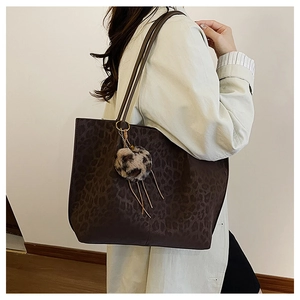Detail of a large leopard print tote bag with a matching plush charm on a slim shoulder strap
