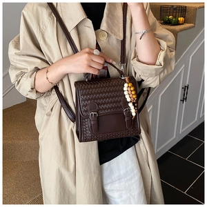 Detail view of brown woven texture bag with vintage buckles and wooden bead charm
