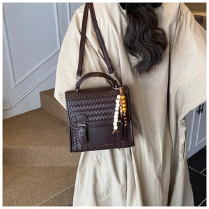 Detail of dark brown woven flap shoulder bag with silver buckles and wooden bead charm