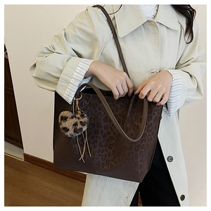 Detail of large leopard print tote bag with heart plush charm worn by model