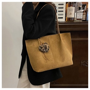 Detail shot of camel suede tote bag with leopard print heart pendant on a model