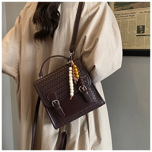 Close-up of brown woven texture handbag with vintage buckle and bead charm detail