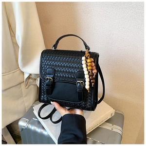 Detailed close-up of a black woven crossbody bag with silver buckles and wooden bead charm