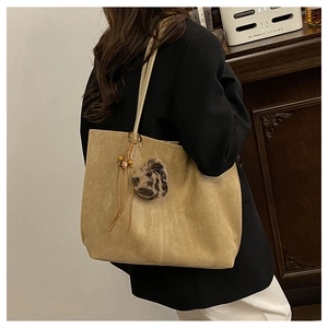 Detail view of large brown suede tote bag with leopard print pom-pom and fringe tassel