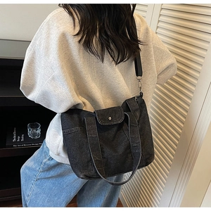 Detail of black denim tote bag with adjustable shoulder strap worn by a model