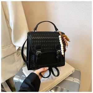 Detail of black woven leather handbag featuring silver buckles and beaded strap charm