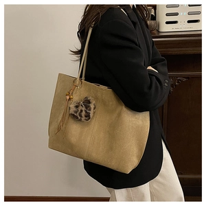 Detail of khaki suede tote bag featuring heart leopard charm and stylish leather tassels