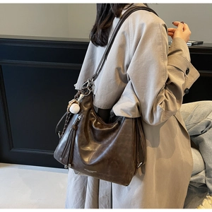 Detail of a large vintage brown tote bag with fringe and baseball charms on a model