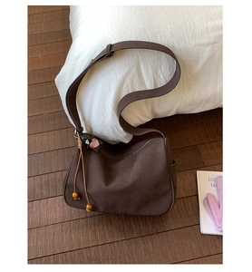 Detail einer dunkelbraunen Wildleder-Schultertasche mit Holzperlen und Trageriemen