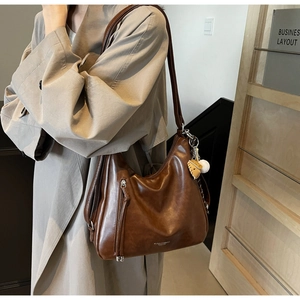 Detailed side view of brown faux leather tote bag with leaf charm and vertical zipper