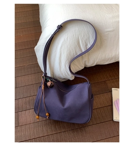 Makro-Detail der lila Nylon-Hobo-Tasche mit Bärenanhänger auf dunklem Holzbodenhintergrund