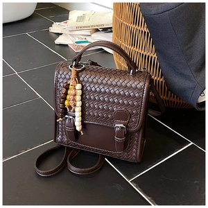Detailed view of dark brown woven leather handbag with metallic buckle and beaded charm
