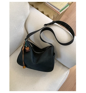 Detail der schwarzen Wildleder Hobo-Tasche mit Quasten auf weißem Sofa