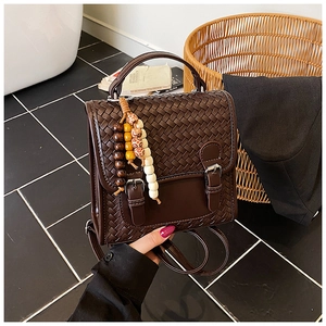 Detail of dark brown woven leather backpack with metal buckles and colorful beaded pendant