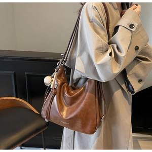 Brown leather tote bag with baseball charm detail and curved zipper, worn with khaki coat