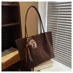 Close-up of retro brown suede tote bag featuring leopard pompom and tassel details