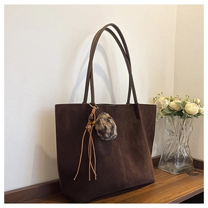 Close-up of brown suede tote bag with leopard print pom-pom and fringe tassel detail