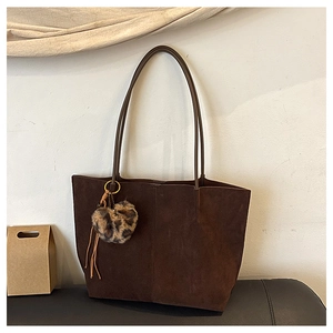 Brown faux suede tote bag featuring a heart-shaped leopard print charm on a leather bench