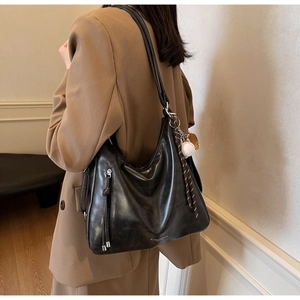 Detail of black leather hobo bag with silver zipper and sporty baseball pendant charm