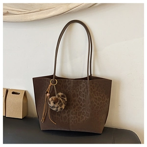 Detail of leopard print tote bag featuring a plush heart charm and slim shoulder straps