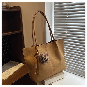 Brown suede tote bag with leopard print pom-pom charm on a sunlit windowsill