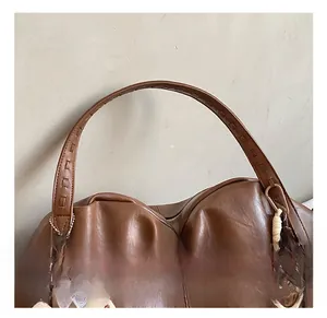Detail of dark brown leather handbag handle with unique square cut-out stitching and plush charm