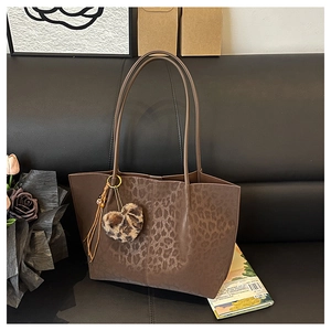 Detailed view of leopard print tote bag with plush heart charm and tassel accessory