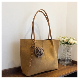 Detail of brown faux suede tote bag featuring leopard pom-pom and tassel decor