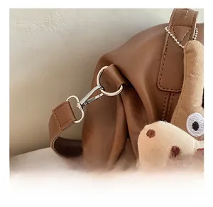 Detailed shot of silver metal hook hardware and plush pendant on brown leather handbag