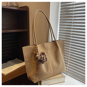 Detail of a khaki suede tote bag with leopard print pompom and tassel on a vintage desk