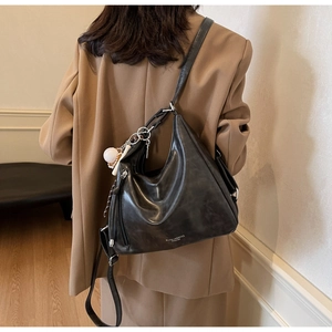 Side view of large black leather hobo bag with silver hardware and baseball charm on model