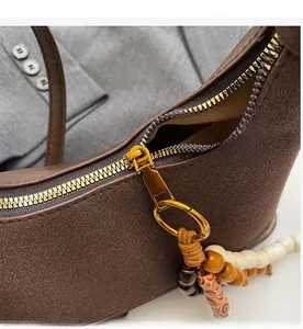 Gros plan sur la fermeture dorée et les perles vintage sur le sac en daim marron