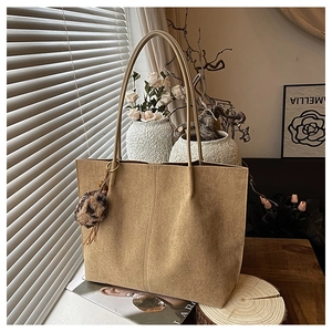 Detail view of khaki suede tote bag with leopard print pompom charm in warm setting