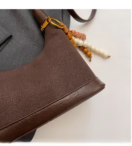 Détail du sac croissant en daim marron foncé avec bordure en cuir et perle décorative